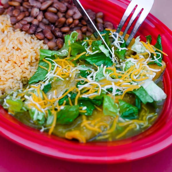 Mexican enchiladas with green sauce, lettuce, cheese, rice, and beans in a red bowl.