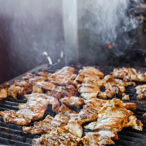 Chicken pieces with grill marks cooking on a smoky grill at Baja Taqueria.