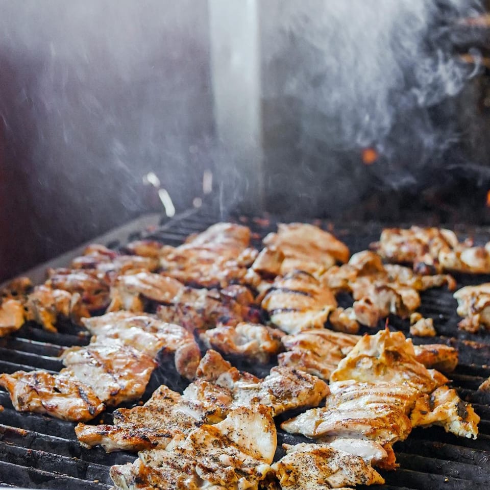 Chicken pieces with grill marks cooking on a smoky grill at Baja Taqueria.