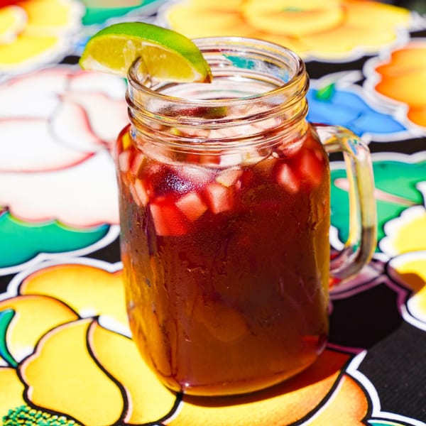 A refreshing red drink with fruit chunks and a lime wedge in a mason jar on a colorful table.