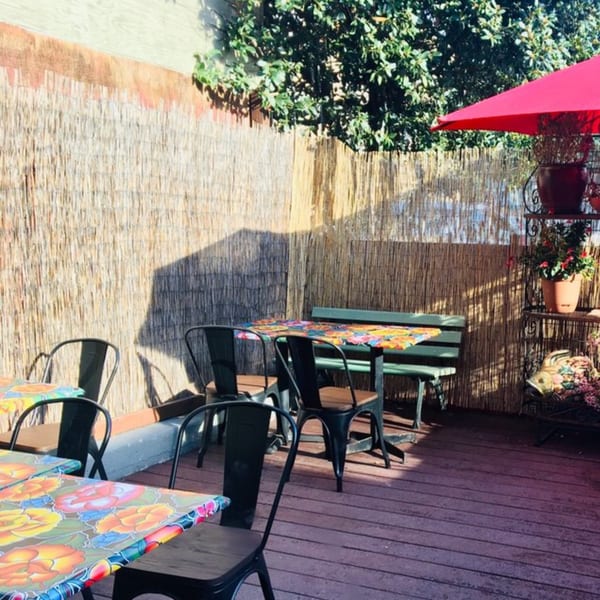 Outdoor patio at Baja Taqueria with colorful tables, black chairs, a red umbrella, and bamboo fencing.
